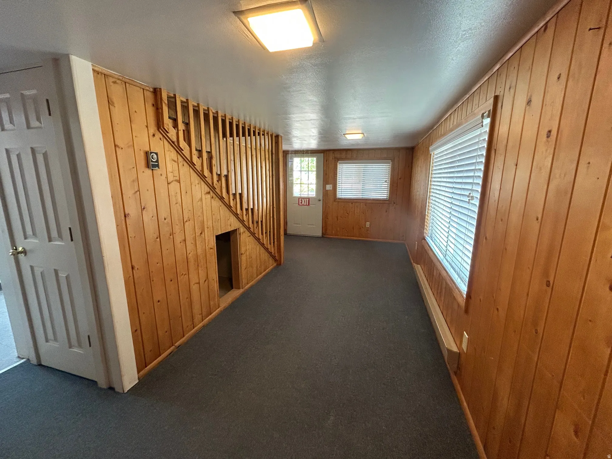 Interior space featuring wood paneling, gray carpeting, a staircase with wood balusters, and multiple windows with blinds