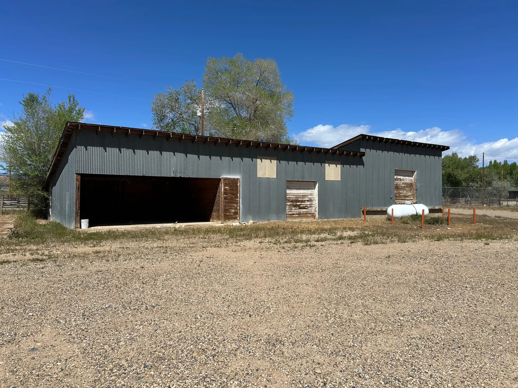 Corrugated metal structure featuring an open bay, multiple exterior doors, and a sloped roofline
