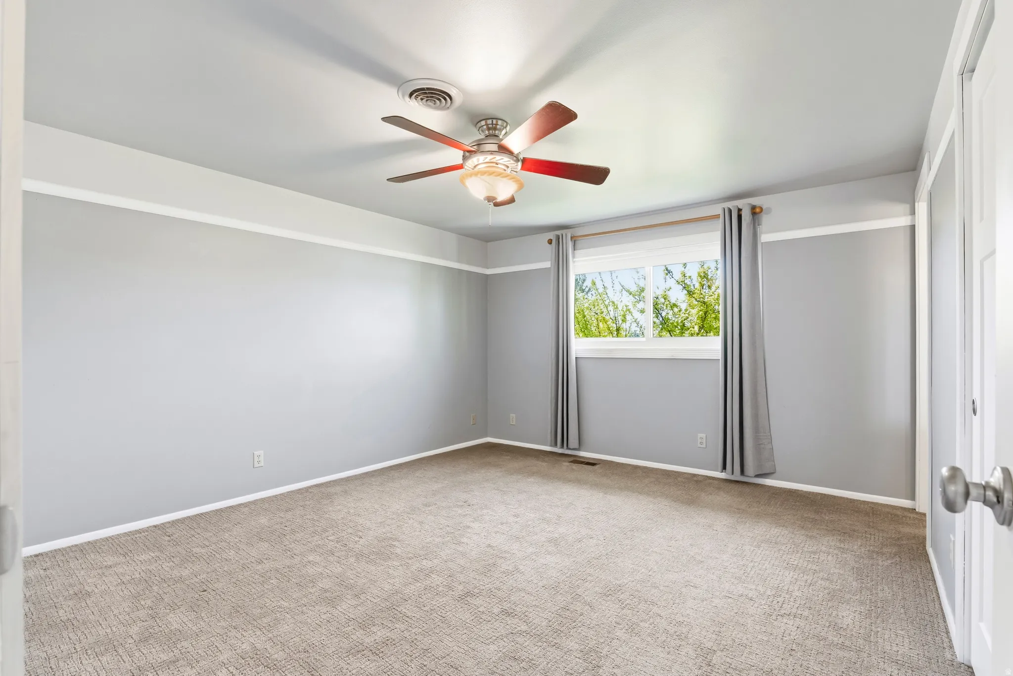 Room featuring neutral gray walls with white trim, a brown carpeted floor, and a ceiling fan with integrated lighting