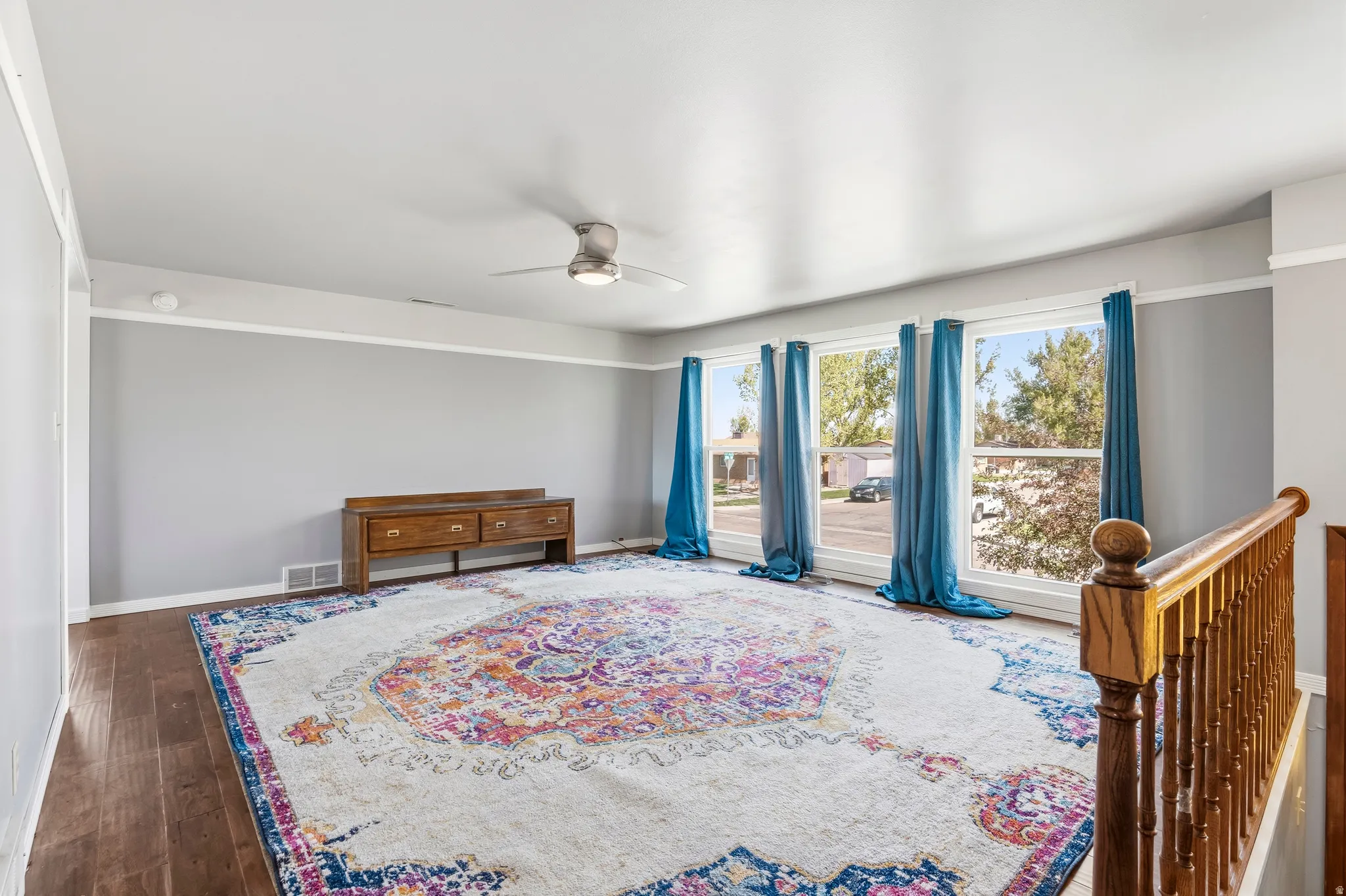 Spacious room featuring wood-finish flooring, light grey walls with white trim, and multiple large windows