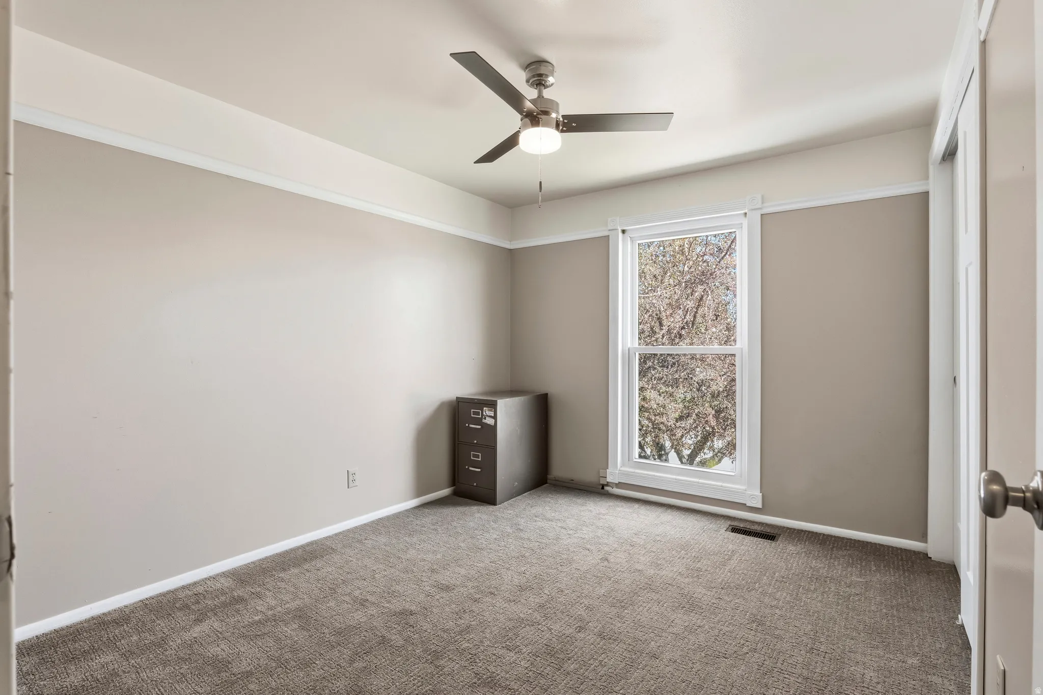 Bright room featuring neutral wall tones, white trim, a ceiling fan with integrated lighting, and carpet flooring