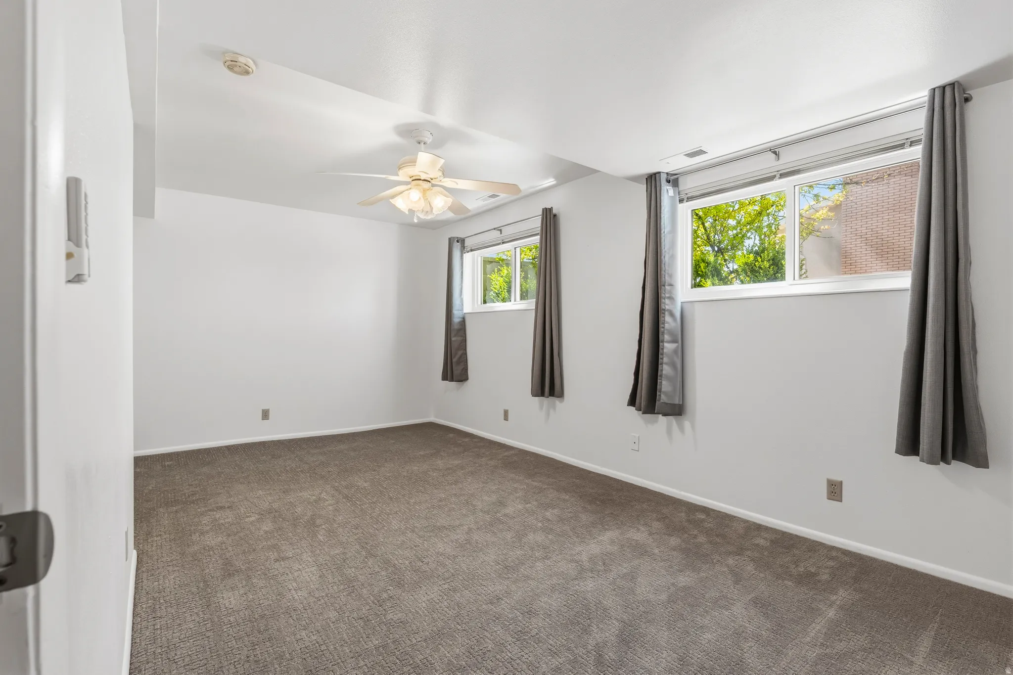 Spacious room featuring neutral carpeting, white walls, two window units, and a ceiling fan with integrated lighting