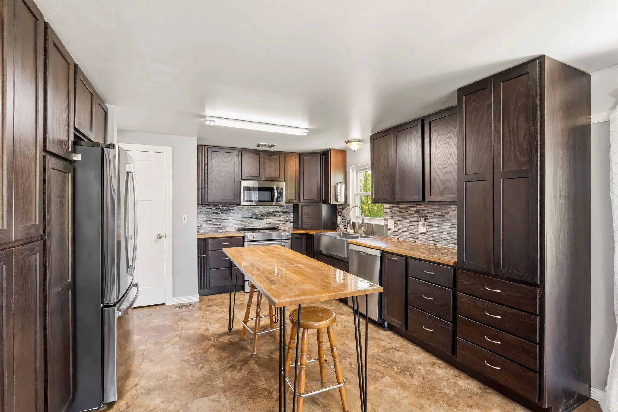 Spacious kitchen featuring dark wood cabinetry, stainless steel appliances, a mosaic tile backsplash, wood-finish countertops, and durable flooring