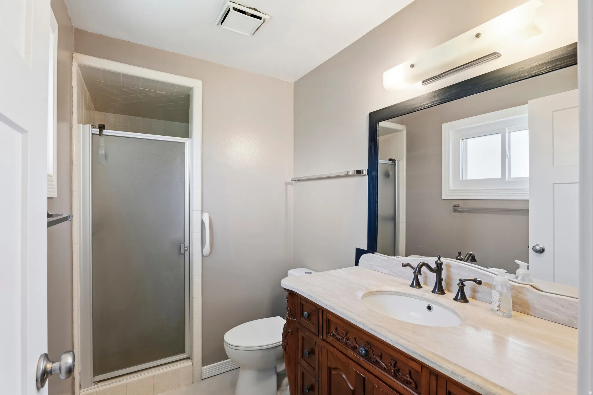Bathroom featuring a shower stall with frosted glass door, a vanity with an integrated sink, a stone-finish countertop, and decorative wood-finish cabinetry