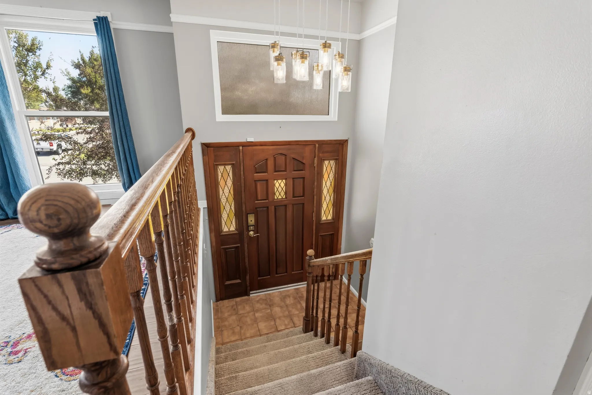 Two-story foyer featuring a wood entry door with decorative glass, a contemporary multi-light pendant fixture, a transom window, wood railing, and carpeted stairs