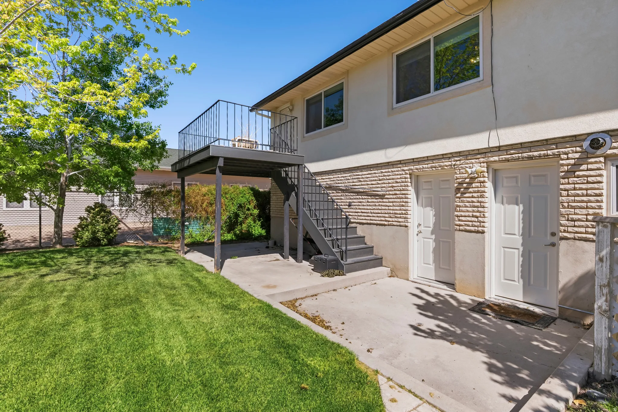 Expansive rear yard featuring a manicured lawn, concrete patio, and mature trees