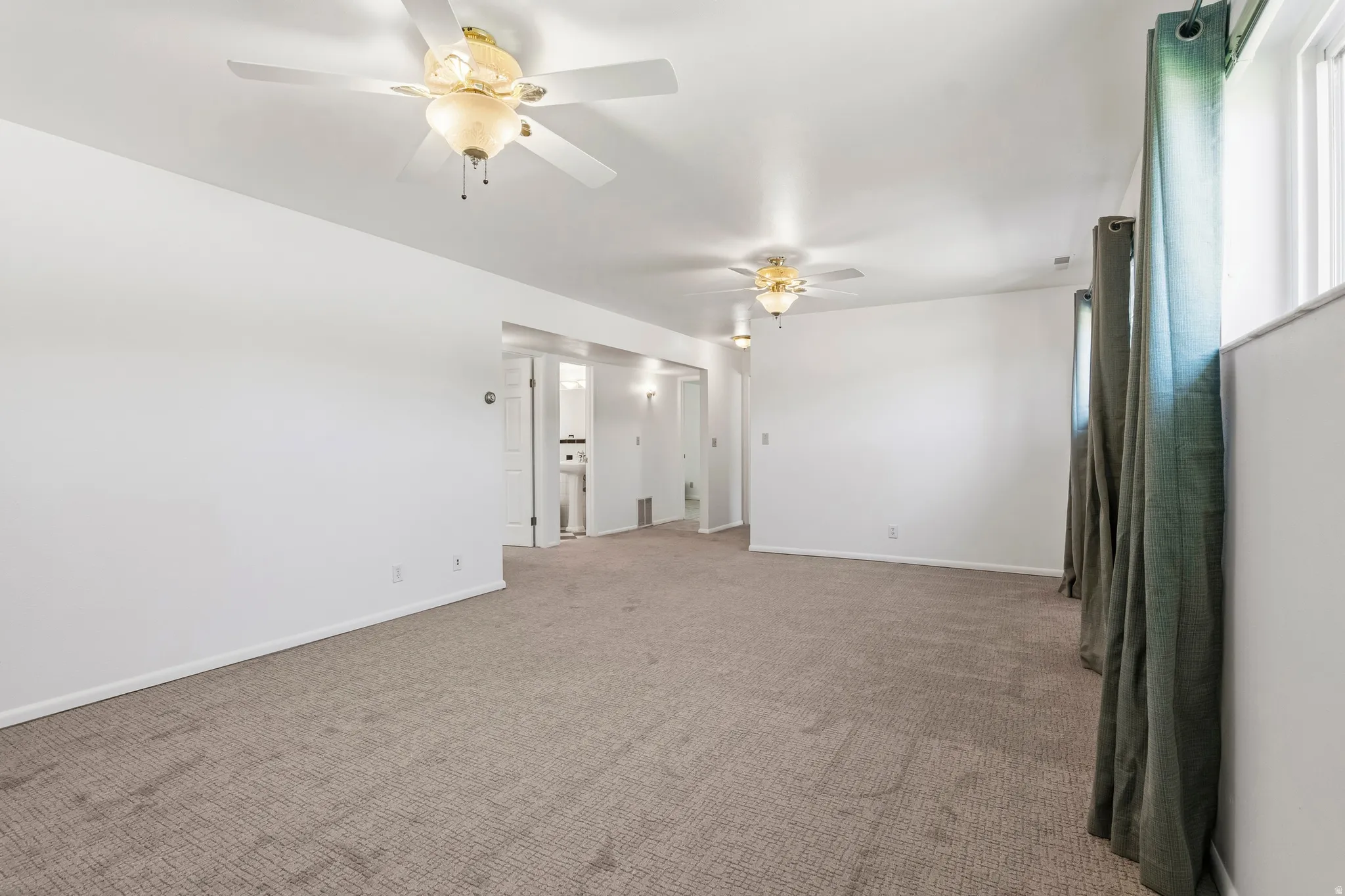Spacious room featuring neutral carpeting, white walls, and two ceiling fans with integrated lighting
