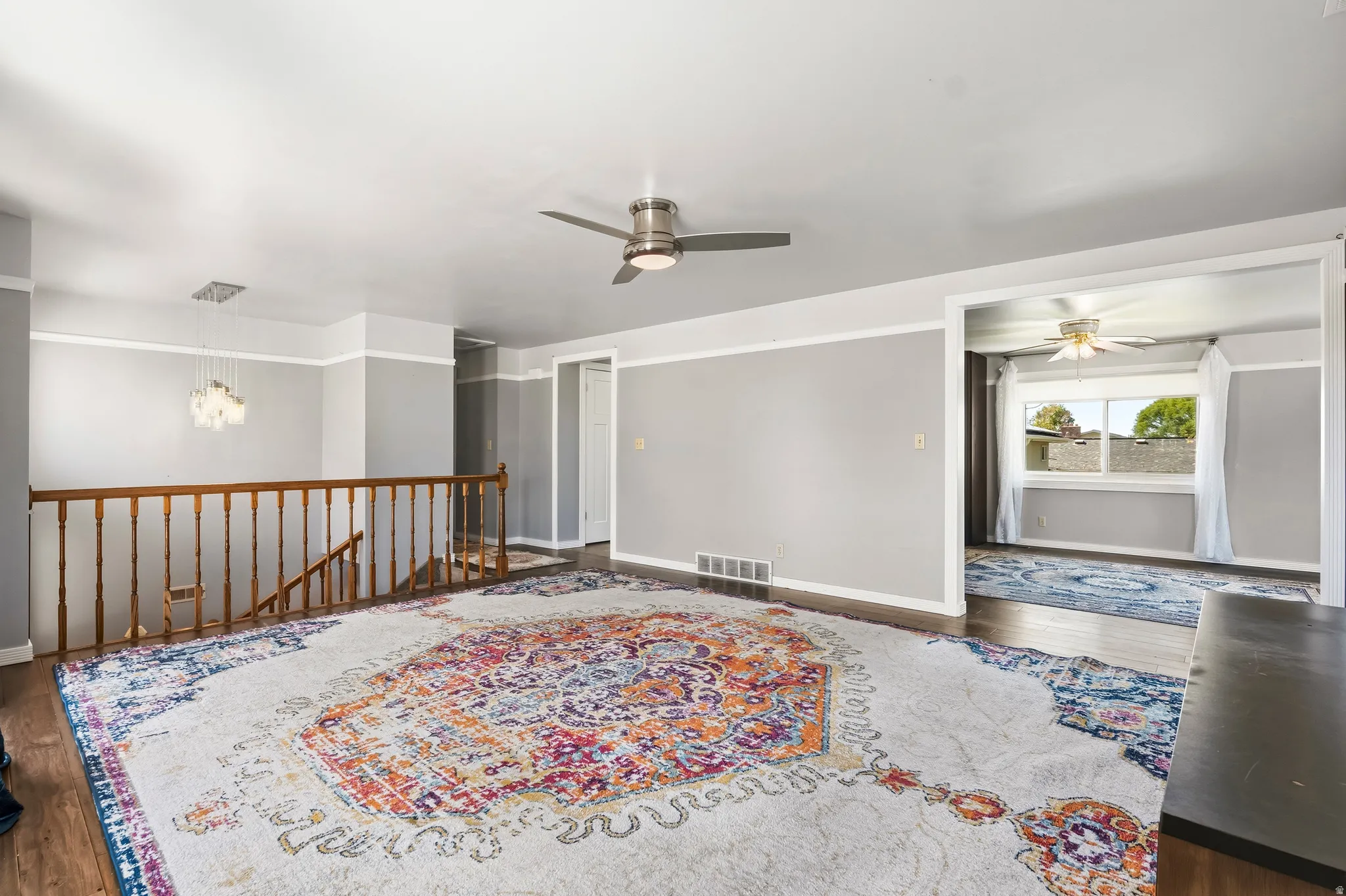 Expansive interior space featuring wood-finish flooring, a contemporary ceiling fan, and a chandelier