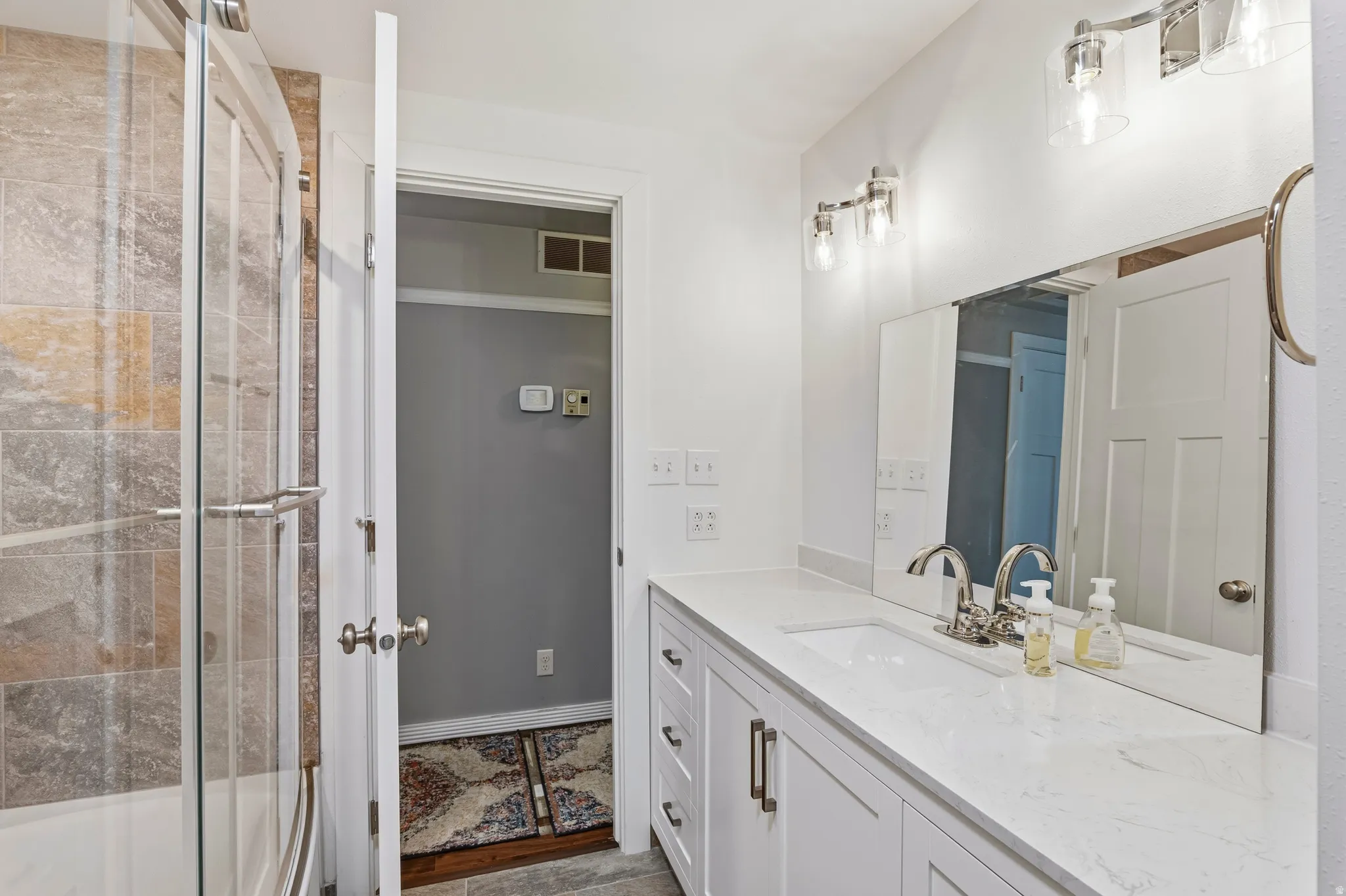 Modern bathroom featuring a tiled shower with a glass enclosure, a double vanity with a light-toned countertop, dual undermount sinks, and polished chrome fixtures