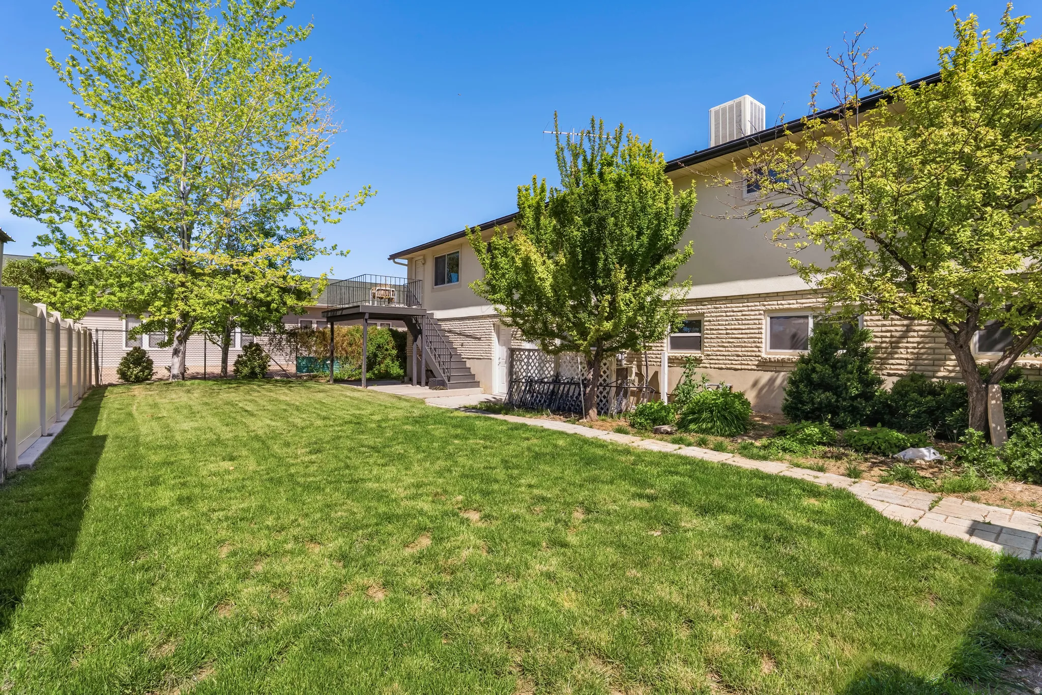 Expansive green lawn bordering a stone walkway, mature trees, and landscaping