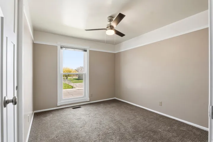 Carpeted room featuring a ceiling fan with integrated lighting, a double-hung window, and neutral wall tones