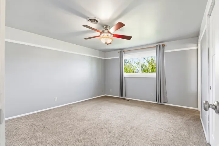 Room featuring neutral gray walls with white trim, a brown carpeted floor, and a ceiling fan with integrated lighting