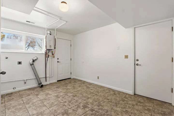 Utility room featuring tiled flooring, a window, a tankless water heater, and a flush-mount ceiling light fixture