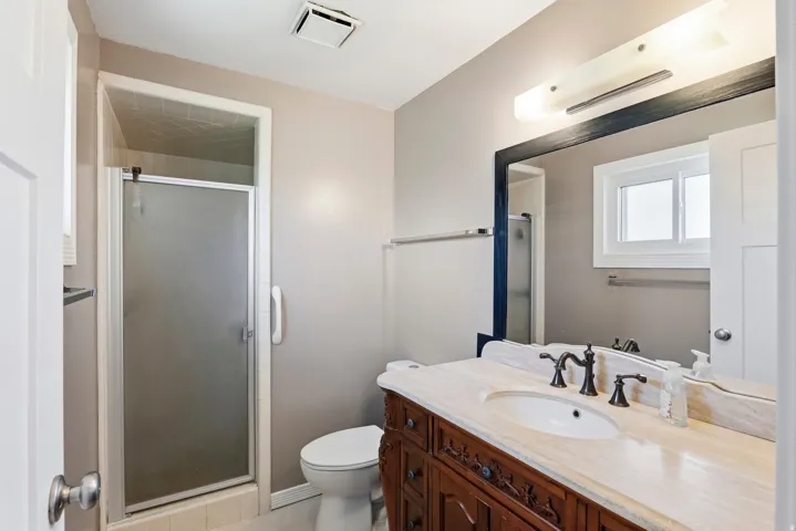 Bathroom featuring a shower stall with frosted glass door, a vanity with an integrated sink, a stone-finish countertop, and decorative wood-finish cabinetry