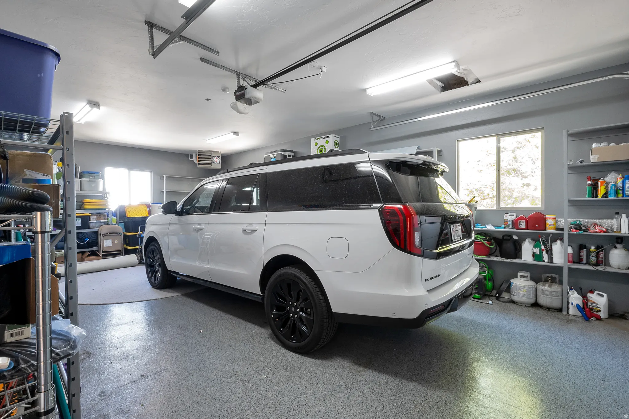 Spacious garage featuring a durable epoxy floor, overhead fluorescent lighting, a built-in shelving system, an automatic garage door opener, and multiple windows