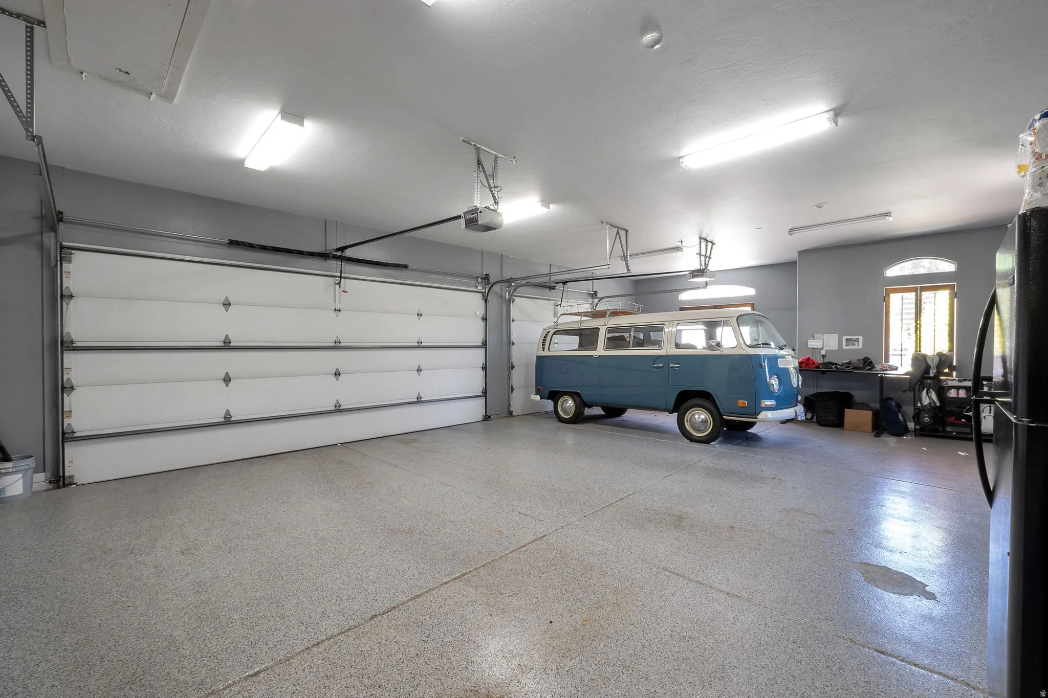 Spacious garage featuring a durable epoxy floor coating, two overhead garage doors, ample overhead lighting, and an arched window