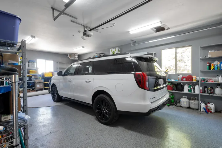 Spacious garage featuring a durable epoxy floor, overhead fluorescent lighting, a built-in shelving system, an automatic garage door opener, and multiple windows