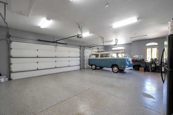 Spacious garage featuring a durable epoxy floor coating, two overhead garage doors, ample overhead lighting, and an arched window
