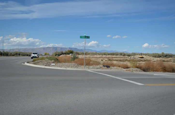 Paved road at an intersection, featuring a street sign, curb, and visible mountainous backdrop