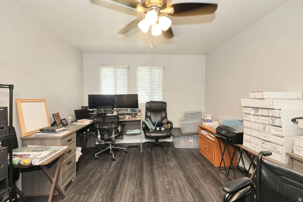 Spacious room featuring wood-finish flooring, two windows with blinds, a ceiling fan with integrated lighting, and light-toned walls