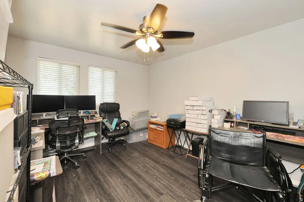 Interior room featuring wood-finish flooring, two windows with blinds, a ceiling fan with integrated lighting, and neutral wall paint
