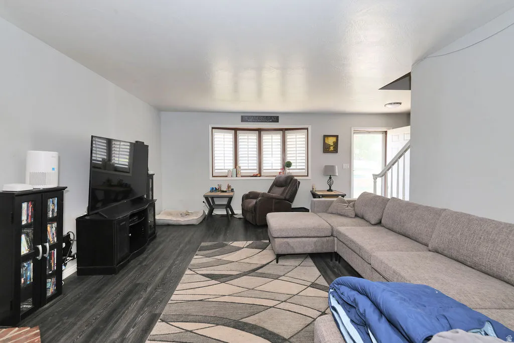 Living area featuring wood-finish flooring, white walls, and a window with white louvered blinds