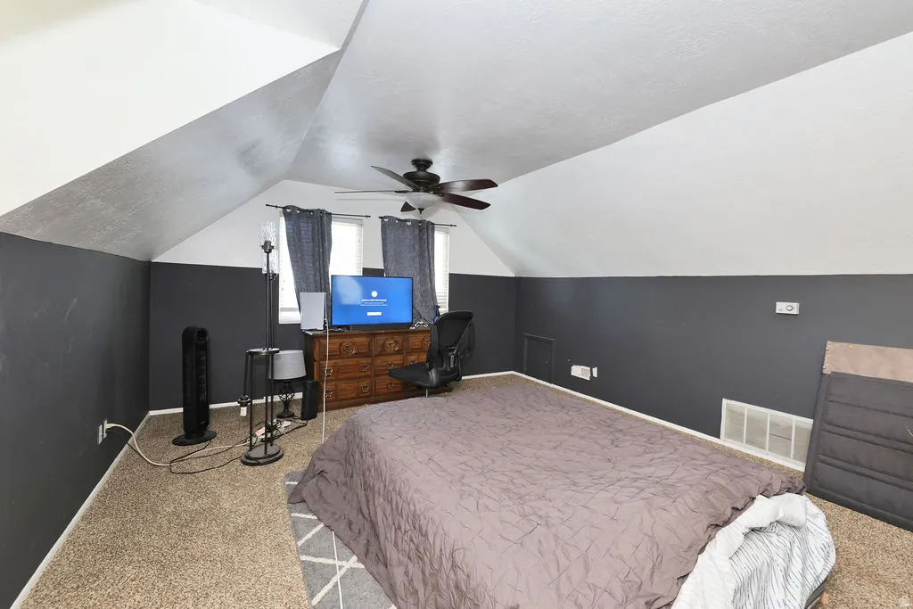 Spacious room featuring sloped ceilings, two windows with dark curtains, and a ceiling fan