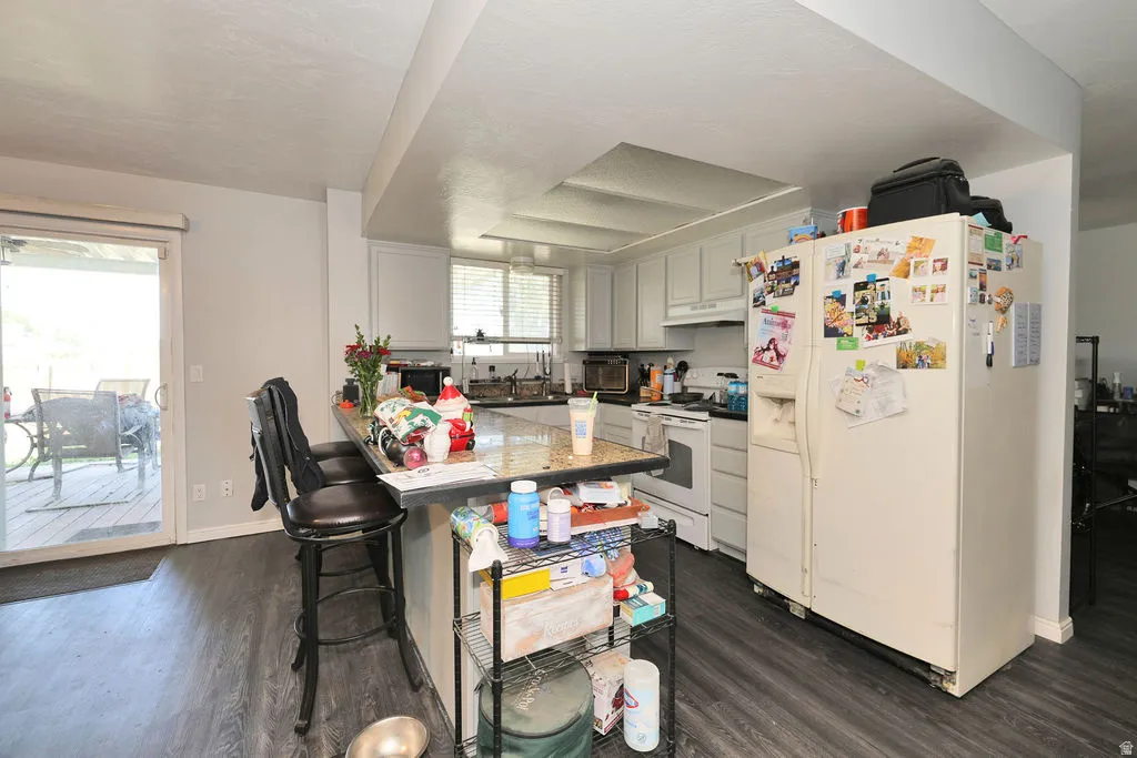 Kitchen featuring a breakfast bar with granite-look countertop, white cabinetry, and wood-finish flooring