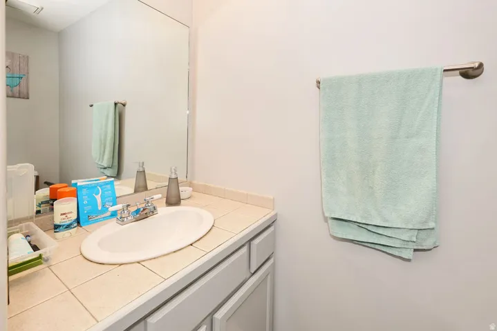 Bathroom vanity featuring a tiled countertop, integrated oval sink, and a chrome-finish faucet