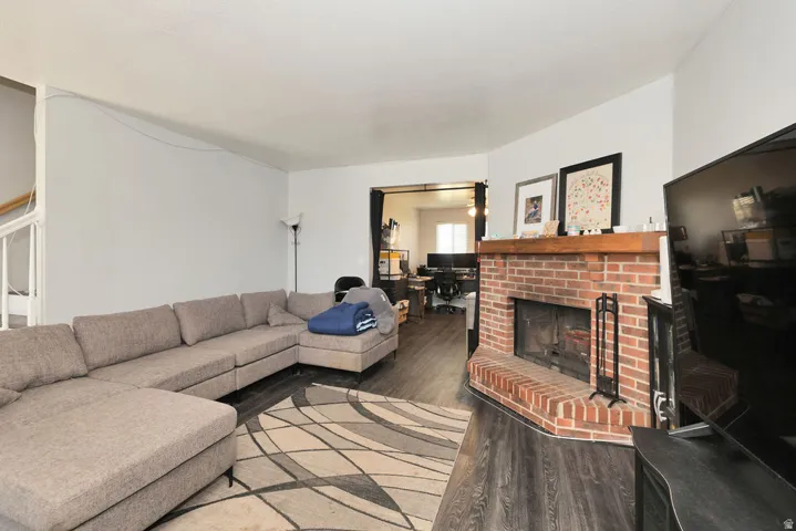 Living area featuring wood-finish flooring, a corner brick fireplace with a wood mantle, and a white painted staircase
