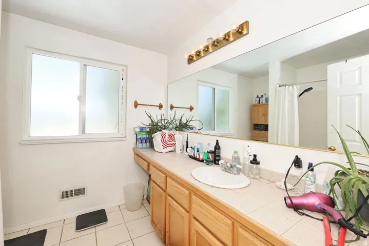 Bathroom featuring a tile countertop vanity with a single sink, a large wall-mounted mirror, and a multi-bulb light fixture
