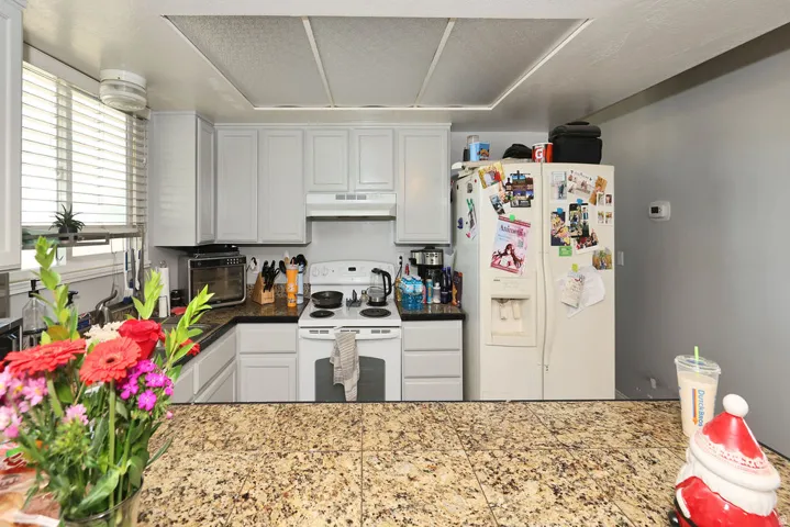 Kitchen featuring upper and lower cabinetry, a corner sink with a window, a white electric range, and a side-by-side refrigerator