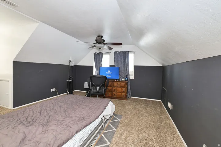 Carpeted room with a ceiling fan, sloped ceilings, and two windows with blinds and curtains