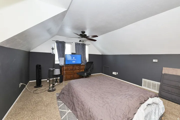 Spacious room featuring sloped ceilings, two windows with dark curtains, and a ceiling fan