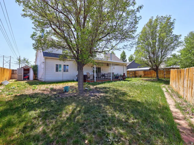 Spacious backyard featuring a covered patio, mature trees, wood fence, and an outdoor storage shed