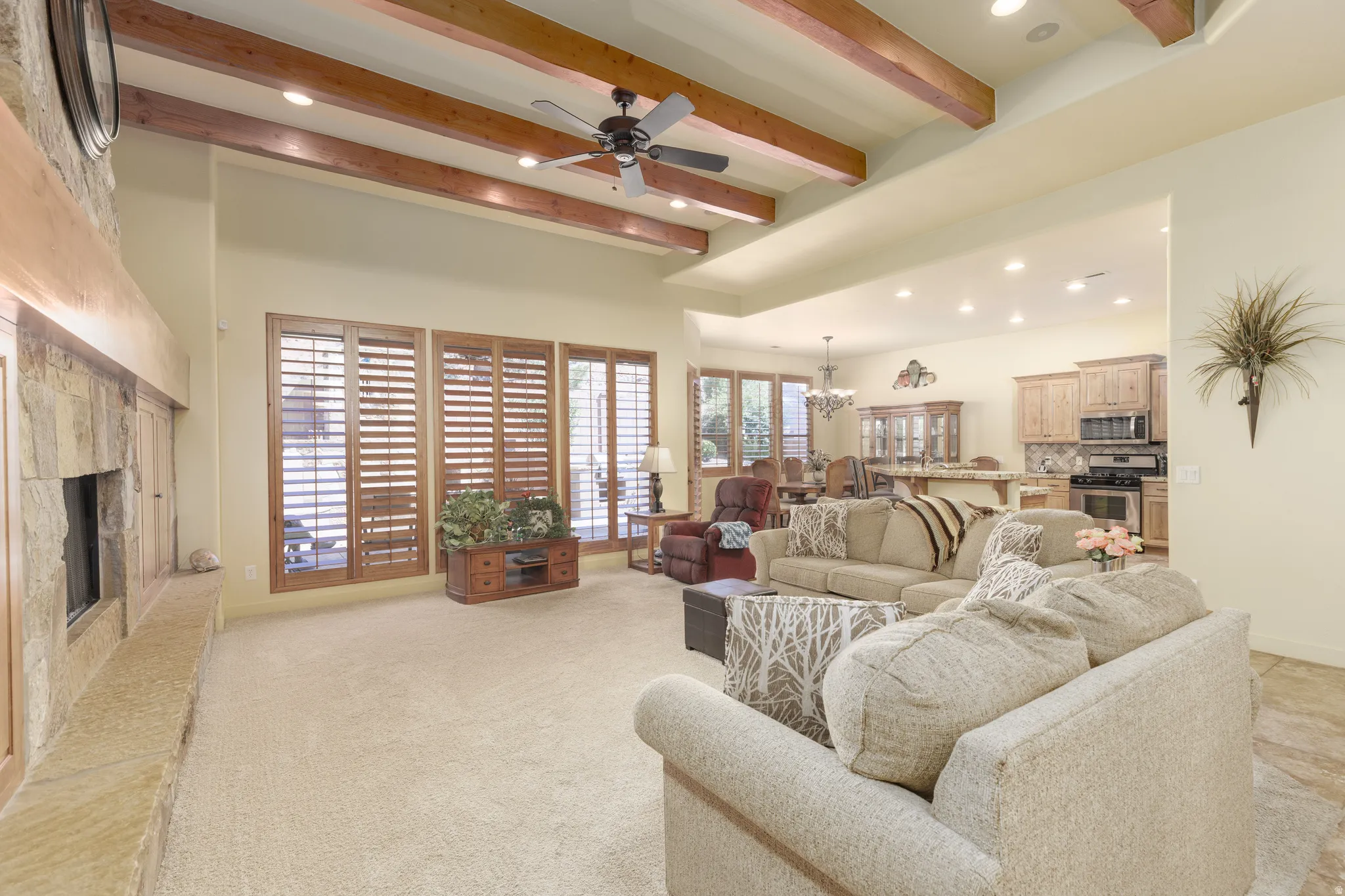 Spacious living area featuring exposed wood beams, recessed lighting, a ceiling fan, and a stone fireplace with a mantle