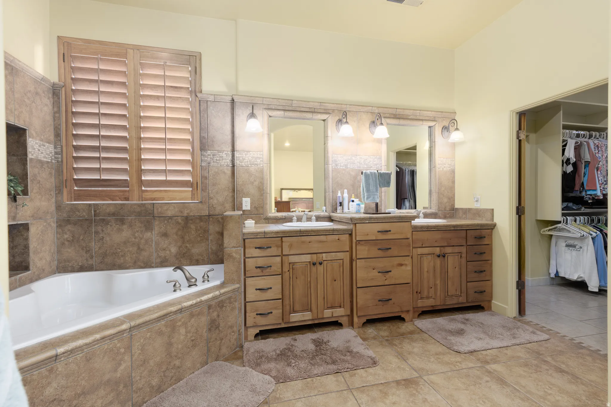 Spacious bathroom featuring a corner soaking tub with tile surround, two built-in shelving niches, and wood plantation shutters