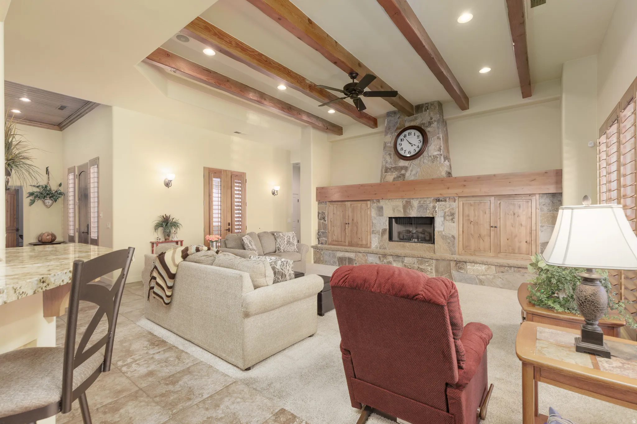 Spacious living area featuring a stone-clad fireplace with built-in cabinetry, wood-beam ceiling accents, recessed lighting, and tile flooring