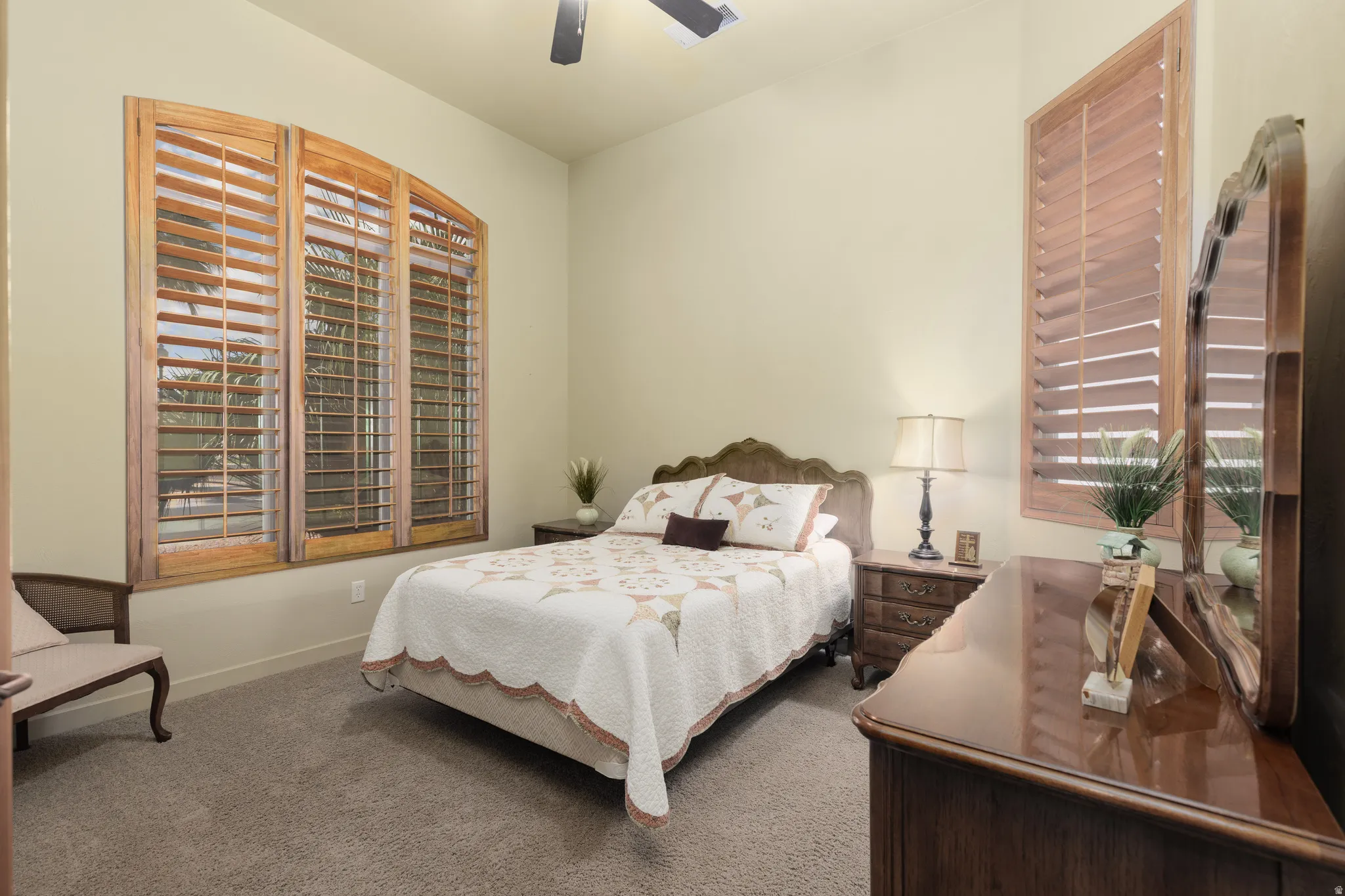 Carpeted room featuring a ceiling fan, arched window with wood plantation shutters, and a vertical window with wood plantation shutters