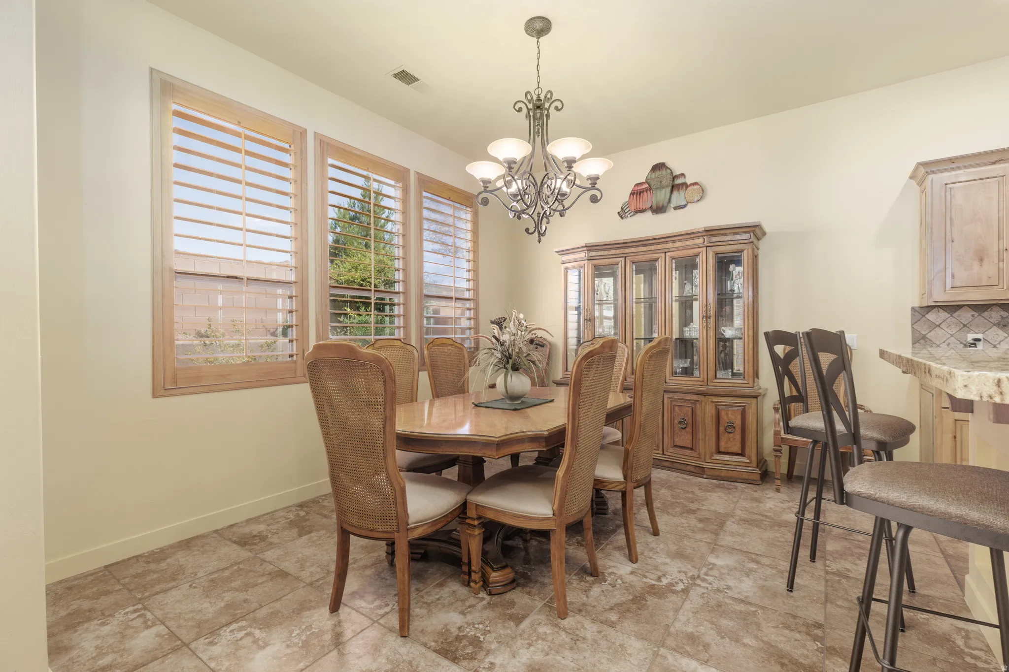 Dining area featuring tile flooring, three large windows with wooden plantation shutters, and a decorative chandelier