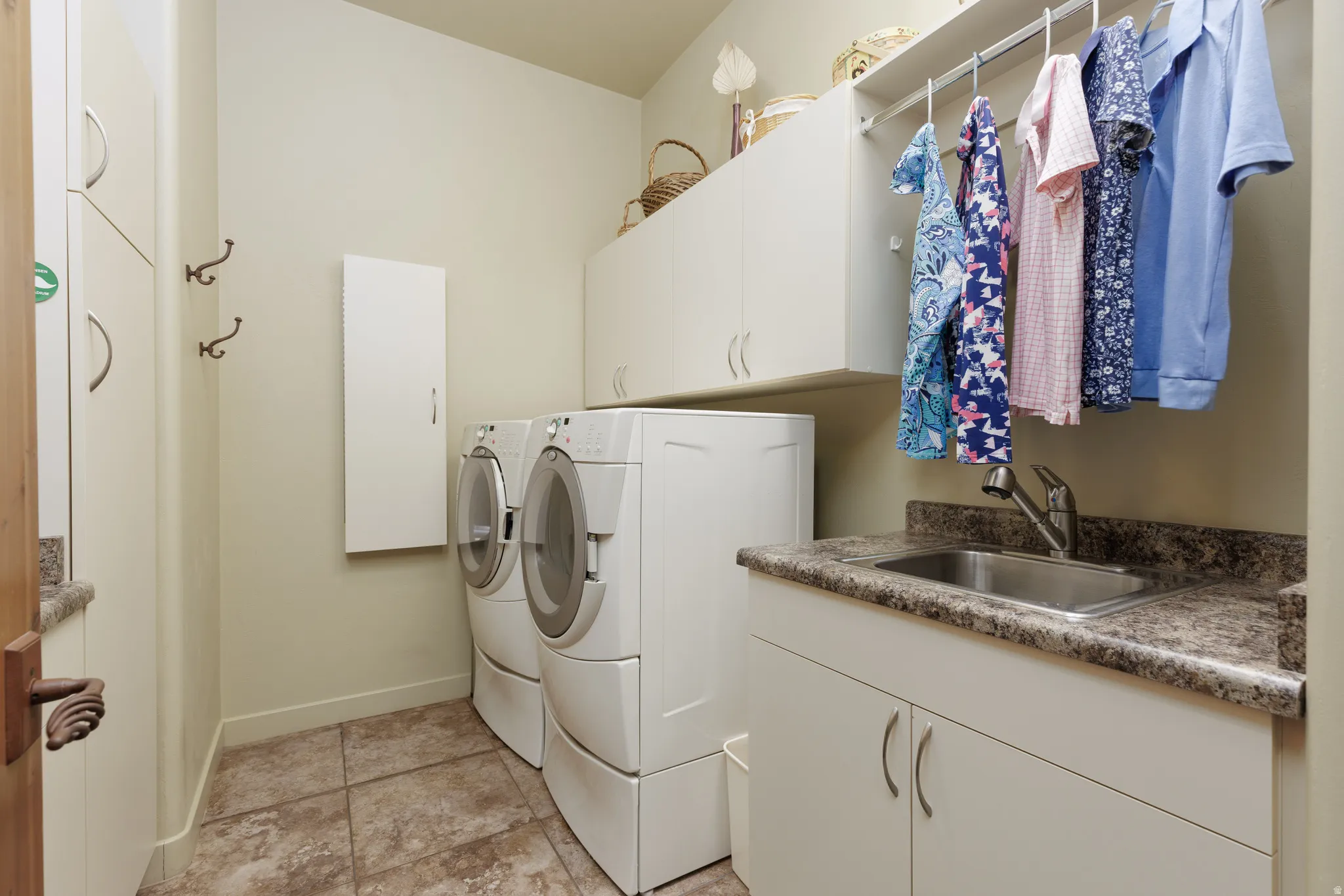 Dedicated utility space featuring stacked front-load laundry appliances, extensive upper and lower cabinetry, a built-in stainless steel utility sink, and tile flooring