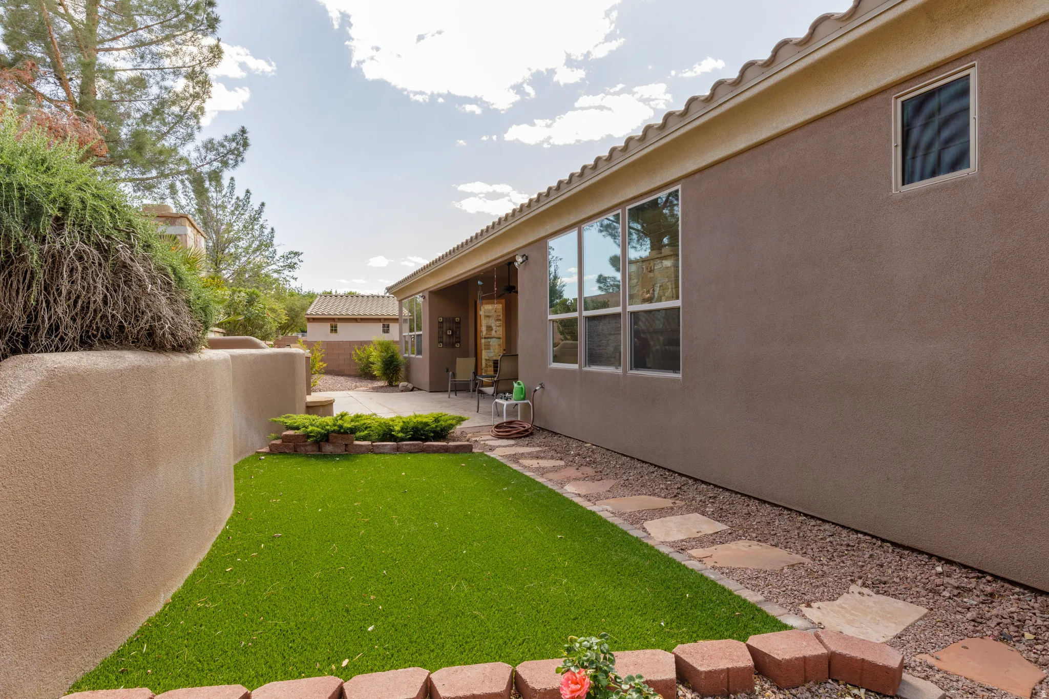 Outdoor space featuring a stucco retaining wall, artificial turf, and a paver stone pathway