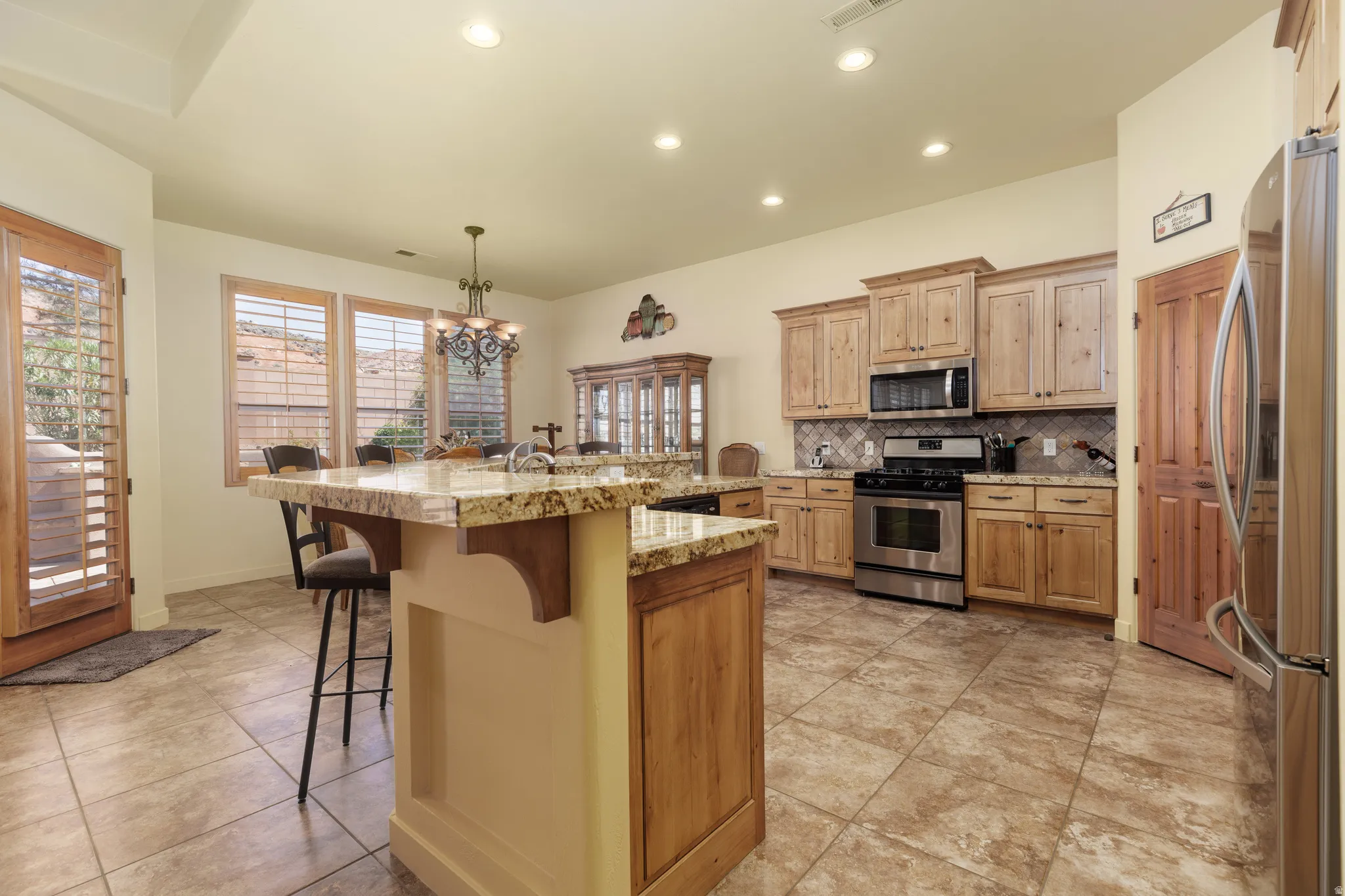 Spacious kitchen featuring an expansive island with granite countertops, light wood cabinetry, stainless steel appliances, and tile flooring