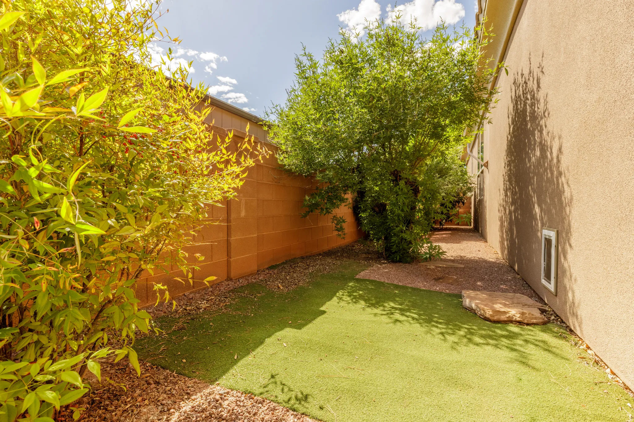 Landscaped side yard featuring artificial turf, decorative gravel, and established plantings