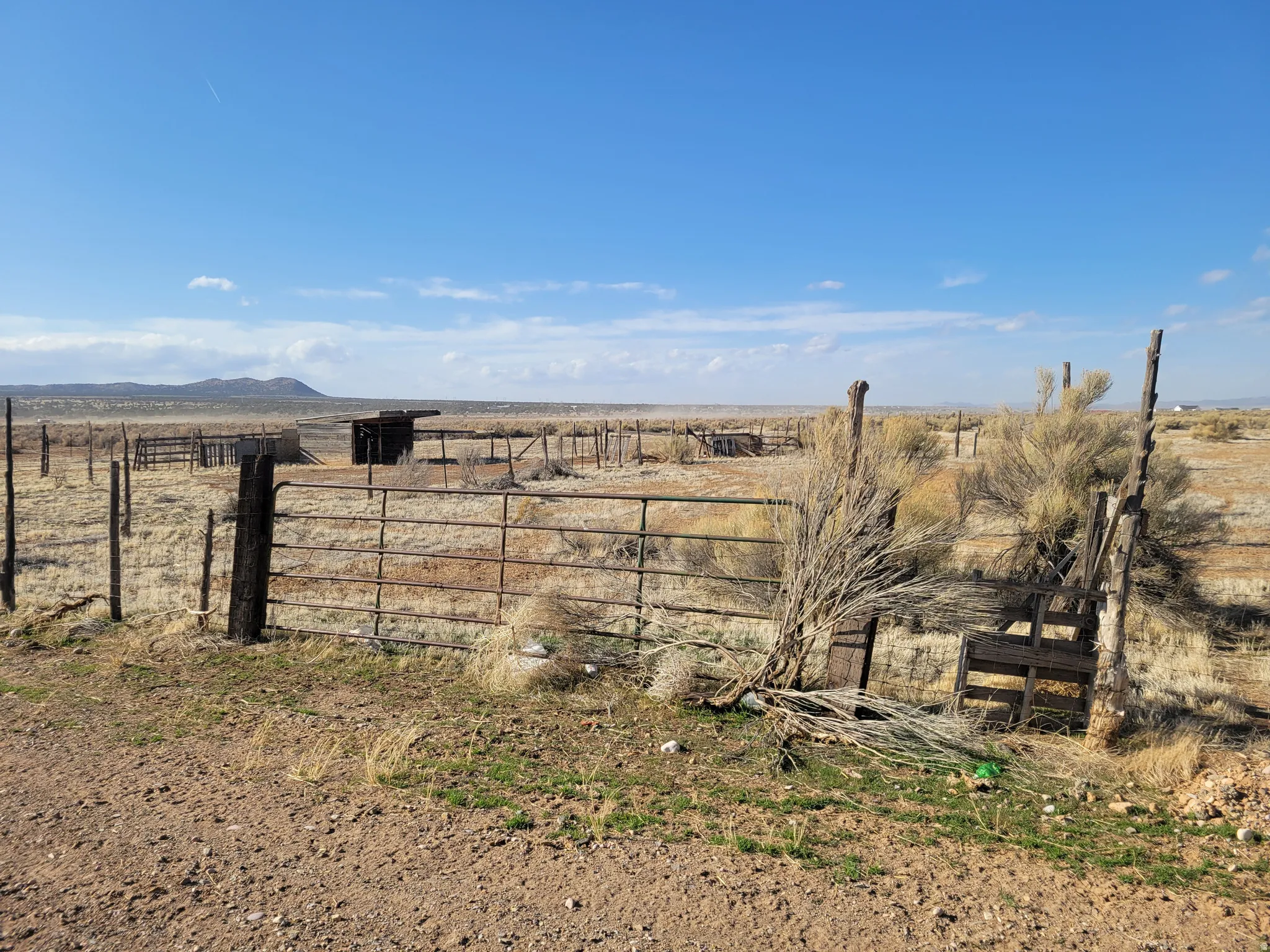 Expansive open terrain featuring a metal fence, wooden posts, and a distant mountain range under a clear sky
