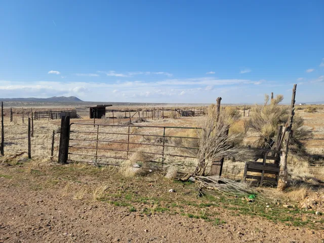 Expansive open terrain featuring a metal fence, wooden posts, and a distant mountain range under a clear sky