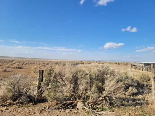 Expansive desert landscape featuring natural brush, a rustic wooden fence, and distant outbuildings under a clear blue sky