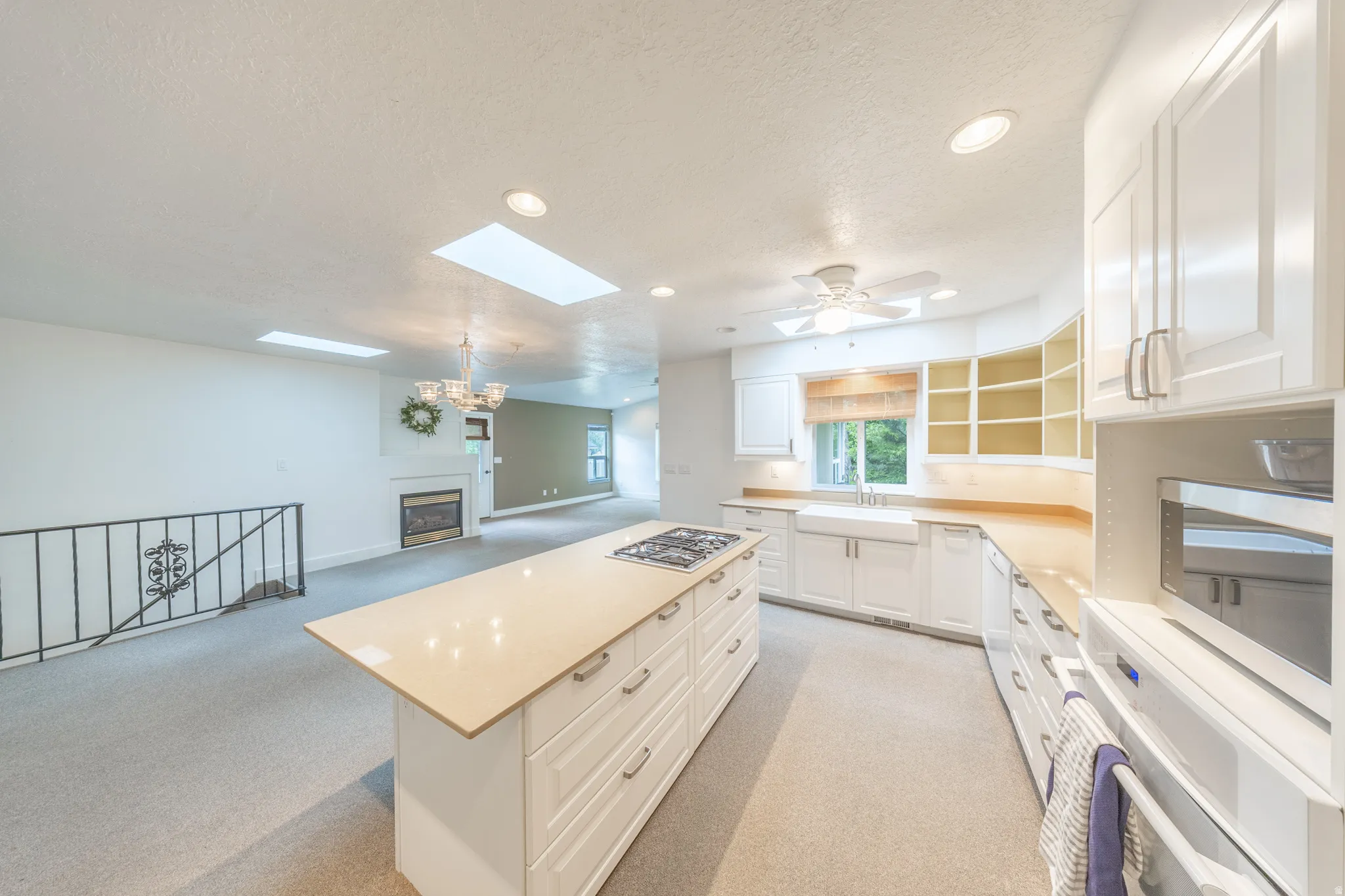 Large kitchen featuring a central island with a built-in gas cooktop, white shaker-style cabinetry, a farmhouse sink, and granite countertops.