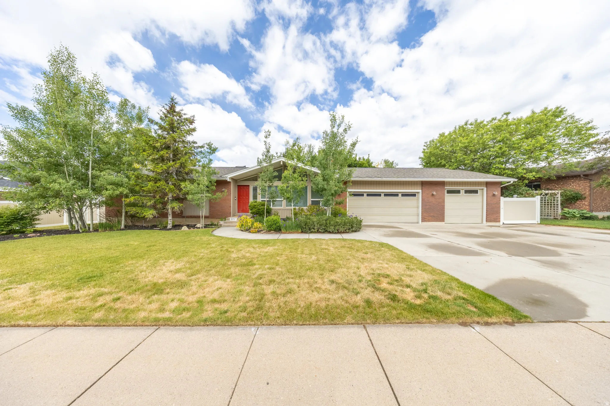 Brick exterior featuring a red entry door, three-car garage, and mature landscaping