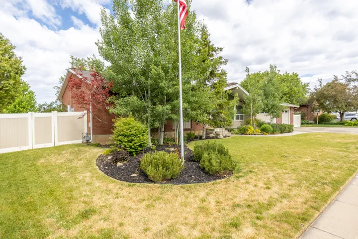 Mature landscaping and a manicured lawn frame the property, featuring a brick exterior and a white vinyl fence